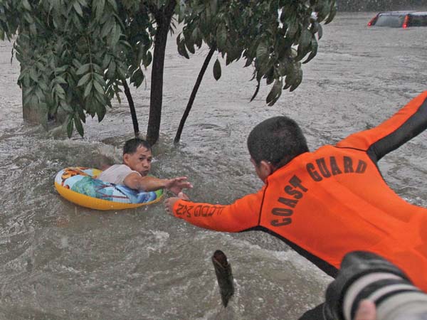 A Coast Guard member reaches out to rescue a man who had clung to a tree for hours after swirling floodwaters swept him away along E. Rodriguez Avenue in Quezon City on Tuesday. MARIANNE BERMUDEZ