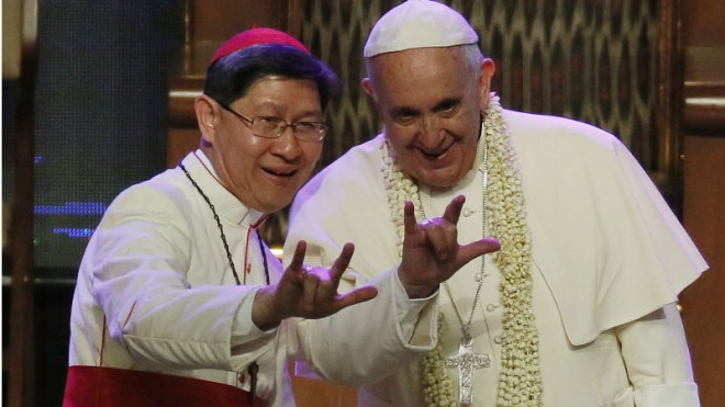 Filipino Cardinal Luis Antonio Tagle, left, shows Pope Francis how to give the popular hand sign for "I love you" at the Mall of Asia arena in Manila, Philippines, Friday, Jan. 16, 2015. Pope Francis is on a five-day apostolic visit in this predominantly Catholic nation in Asia. (AP Photo/Wally Santana)