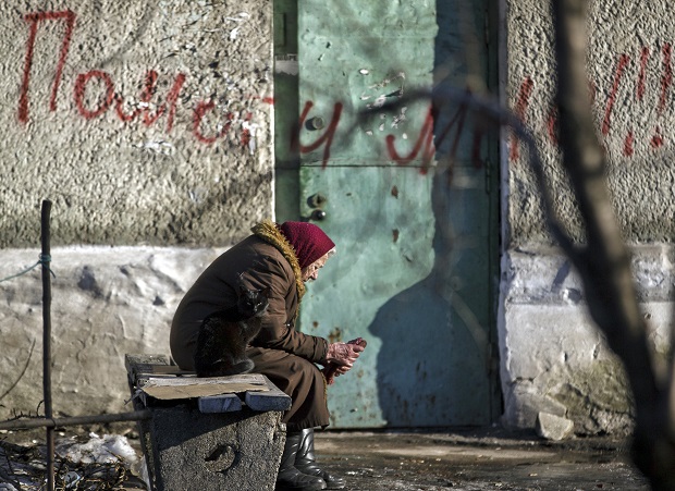 In this Monday, Feb. 23, 2015 photo, an elderly woman and a cat sit on a bench outside a damaged apartment building in Debaltseve, Ukraine. Ukraine delayed a promised pullback of heavy weapons from the front line Monday, blaming continuing attacks from separatist rebels in eastern Ukraine. Writing on the wall reads "Help Me !" (AP Photo/Vadim Ghirda)
