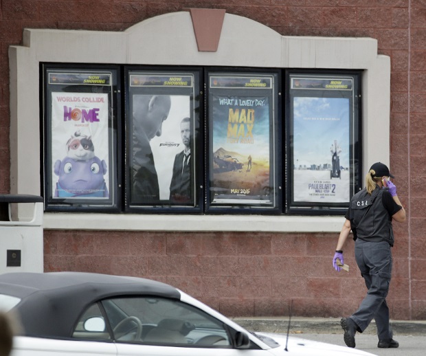 A police officer walks by a display of movie posters, including one for "Mad Max," outside a movie theater following a shooting Wednesday, Aug. 5, 2015, in Antioch, Tenn. A man armed with a hatchet and gun unleashed a volley of pepper spray at audience members inside a movie theater, exchanging fire with a responding officer before being shot dead by a SWAT team as he tried to escape through the theater's rear door, police said. (AP Photo/Mark Humphrey)