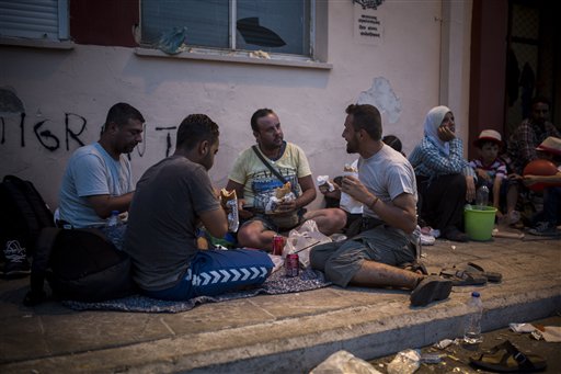 In this photo taken on Monday, Sept. 7, 2015, Mohammed al-Haj from Syria, right, eats a sandwich with friends as he waits to be registered and issued travel documents by local authorities at the port of Mytilene, on the northeastern island of Lesbos, Greece. Mohammed, a 26-year-old from Aleppo, was one of more than 600,000 migrants and refugees who flowed into Europe so far this year. The Associated Press followed Mohammed on nearly every step of his 2,500-mile journey in September, starting from Killis, Turkey, where his family lived for a year after escaping Syria. (AP Photo/Santi Palacios)