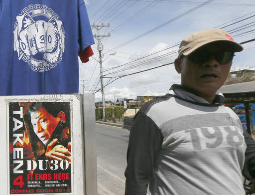In this Wednesday, May 11, 2016 photo, a resident walks past a campaign poster of presumptive President-elect Rodrigo Duterte heralding his anti-criminality and anti-drugs platform is displayed along with souvenir T-shirts along a street at his hometown in Davao city, southern Philippines. AP