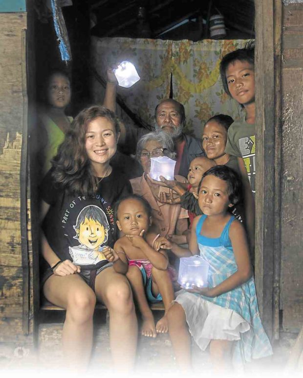 A YOUTH volunteer of One Million Lights-Philippines (OML-PH) joins a family in an impoverished coastal village of Sta. Cruz town, Zambales province that received solar-powered lanterns courtesy of the group OML-PH. CONTRIBUTED PHOTO