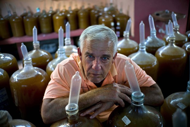 In this March 30, 2017 photo, winemaker Orestes Estevez poses among dozens condom topped wine jugs at his house in Havana, Cuba, Thursday. Estevez and his family fill the glass jugs with grapes, ginger and hibiscus, then slip a condom over each glass neck to start the unusual process of winemaking in a land famed for rum. (AP Photo/Ramon Espinosa)