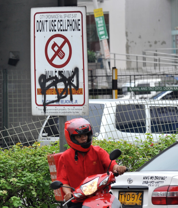 A delivery man speeds past a traffic sign warning motorists against using their mobile phone while driving, displayed on a sidewalk in Manila on January 12, 2011.   AFP PHOTO / TED ALJIBE / AFP PHOTO / TED ALJIBE