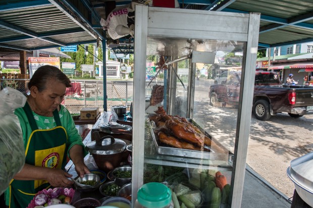 This picture taken on May 4, 2017 shows Mali Pansari, the wife of food vendor Sila Sutharat, preparing garnishes as solar-cooked chicken is displayed on their counter at their eatery in Petchaburi province, south of Bangkok. Not many chefs don a welding mask before they enter the kitchen, but Sila Sutharat prefers to cook his chicken sunny side up. Two hours south of Bangkok this 60-year-old vendor has found an ingenious way to offer his customers something a little different by harnessing the power of the sun. Using a large wall of nearly 1,000 moveable mirrors -- a device he designed and built himself -- he focuses the sun's rays onto a row of marinated chickens, sizzling away under the intense heat. / AFP PHOTO / Roberto SCHMIDT