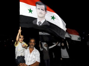 Syrians carry national flags depicting President Bashar Assad, after Assad's interview on state-run TV, in Omawiyeen Square, Damascus, Syria, Sunday, Aug. 21, 2011. Assad said Sunday his regime was in no danger of collapse and warned against any foreign military intervention in his country as the regime tries to crush a 5-month-old popular uprising. AP Photo/Muzaffar Salman
