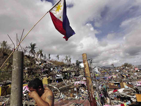 A survivor wipes his face before a Philippine flag in typhoon-ravaged Tacloban, a city short of food and water, and littered with countless bodies.  AP 