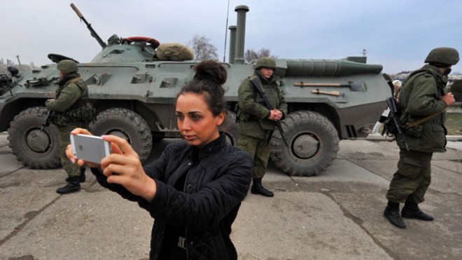 A woman takes photos in front of armed servicemen and their armored personnel carrier in the eastern Crimea's port city of Feodosiya on Sunday, March 2, 2014. Witnesses said Russian soldiers had blocked about 400 Ukrainian marines at a base in the eastern port city of Feodosiya and were calling on them to surrender and give up their arms.  AFP PHOTO/VIKTOR DRACHEV