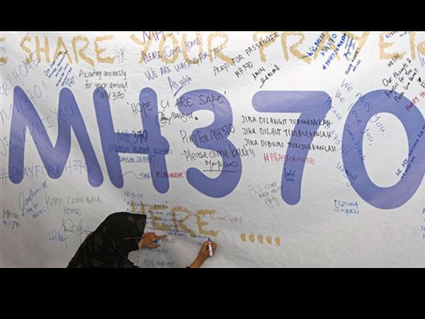 A woman writes a message for passengers aboard a missing Malaysia Airlines plane on a banner at Kuala Lumpur International Airport in Sepang, Malaysia, Wednesday, March 12, 2014. AP.