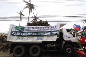 A TRUCK bearing a streamer announcing a cash-for-work program of the Buddhist Tzu Chi Foundation makes its way to communities in need of aid amid debris left by “Yolanda” in Tacloban City.  RICHEL V. UMEL/INQUIRER MINDANAO  