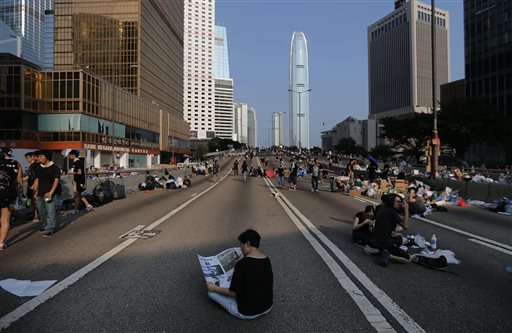 A woman sits and reads the newspaper in the middle of a street which pro-democracy activists have made camp at, Tuesday, Sept. 30, 2014 in Hong Kong. Students and activists, many of whom have been camped out since late Friday, spent a peaceful night singing as they blocked streets in Hong Kong in an unprecedented show of civil disobedience to push demands for genuine democratic reforms. AP