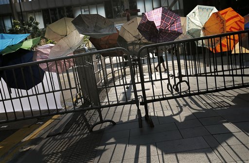 A woman is silhouetted as she walks past a barricade made of metal gates and umbrellas in the central financial district, Tuesday, Sept. 30, 2014, in Hong Kong. Students and activists, many of whom have been camped out since late Friday, spent a peaceful night singing as they blocked streets in Hong Kong in an unprecedented show of civil disobedience to push demands for genuine democratic reforms. (AP Photo/Wong Maye-E)