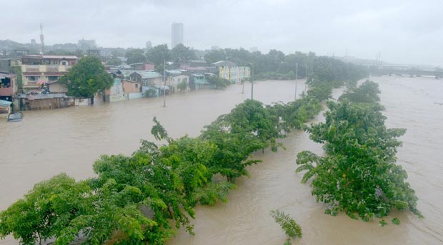 Floods waters from Marikina river (R) overflows to a street along the river and residences (L) in the suburbs of Manila on September 19, 2014. Heavy rains brought by the outer bands of Tropical Storm Fung-Wong shut down the Philippine capital on September 19, stranding motorists and forcing tens of thousands to flee their flooded homes, officials said. AFP 