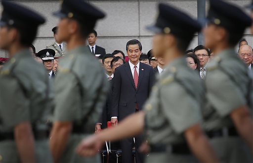 Hong Kong's Chief Executive Leung Chun-ying, center, watches as military personnel march during a flag-raising ceremony on Wednesday, Oct. 1, 2014 in Hong Kong, as thousands of protesters watching from behind police barricades yelled at him to step down. AP