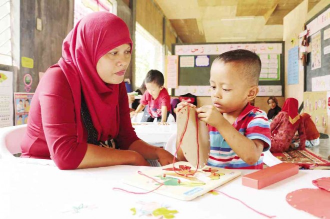 EVELYN Sacurat observes her 3-year-old son, Rainier, accomplish  a learning exercise at the newly established Australian government-assisted Tahderiyyah on Durian Avenue, Barangay Madaum, Tagum City.      Photo: KENNY NODALO/ CONTRIBUTOR