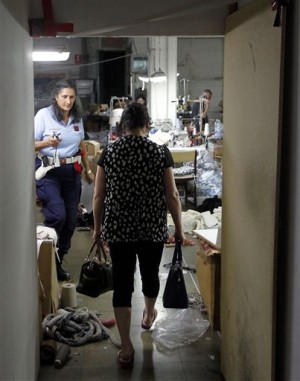 In this June 19, 2014 photo, a police officer, left, takes pictures as a woman walks by in a sequestered textile factory in Prato, Italy. AP