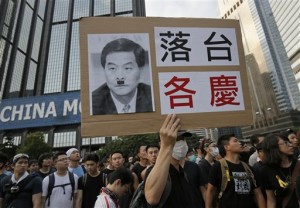 Protesters raises a placard with a deface picture of Hong Kong's Chief Executive Leung Chun-ying outside a flag-raising ceremony where Hong Kong's embattled leader attended in Hong Kong, Wednesday, Oct. 1, 2014, to mark China's National Day. Leung attended the flag-raising ceremony Wednesday to mark China's National Day after refusing to meet pro-democracy demonstrators despite their threats to expand the street protests that have posed the stiffest challenge to Beijing's authority since China took control of the former British colony in 1997. The Chinese words read " Step Down " (AP Photo/Vincent Yu)