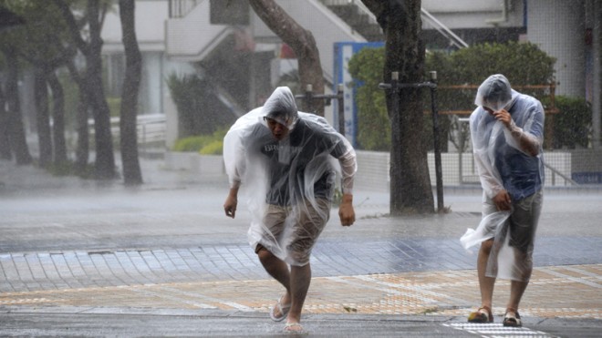 Passersby make their way through strong wind caused by approaching typhoon Vongfong in Naha, Okinawa, southern Japan, Saturday, Oct. 11, 2014. (AP Photo/Kyodo News)