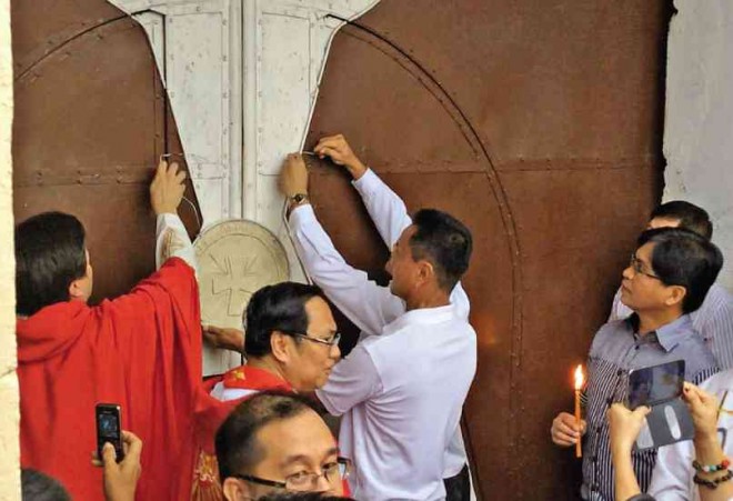 LAOAG Bishop Renato Mayugba (center, with glasses) and Piddig Mayor Eduardo Guillen (right, holding candle) witness the placing of a seal on the door of the 204-year-old St. Anne parish church to symbolize the building’s closure. LEILANIE ADRIANO/INQUIRER NORTHERN LUZON 