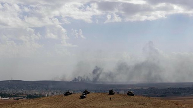 Turkish soldiers in tanks and an armoured vehicle hold their positions on a hilltop in the outskirts of Suruc, Turkey, at the Turkey-Syria border, overlooking smoke rising from a fire caused by a strike in Kobani, Syria, during fighting between Syrian Kurds and the militants of Islamic State group, Thursday, Oct. 9, 2014. Kobani, also known as Ayn Arab, and its surrounding areas, has been under assault by extremists of the Islamic State group since mid-September and is being defended by Kurdish fighters.(AP Photo/Lefteris Pitarakis)