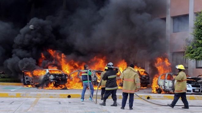 Firefighters try to extinguish burning vehicles in front of the state congress building after protesting teachers torched them in the state capital city of Chilpancingo, Mexico, Wednesday Nov. 12, 2014. Violent protests over the disappearance of 43 college students continue and are now threatening tourism in the nearby resort city ofAcapulco ahead of a major holiday weekend when Mexicans traditionally flock to the beach, business leaders said Wednesday. Investigators say the 43 students from a rural teachers college were rounded up by local police, turned over to a drug gang and apparently killed, their corpses charred into ash and dumped into a river. (AP Photo/Alejandrino Gonzalez)