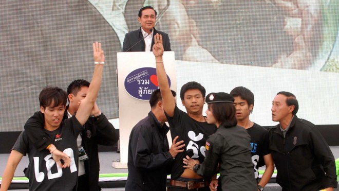 In this Wednesday, Nov. 19, 2014 photo, Thai student activists raise the three-fingered salute in front of Thai Prime Minister Prayuth Chan-ocha speak in Khon Kaen province, northeast of Bangkok, Thailand. Five university students were arrested after giving the salute during the speech by Prime Minister Prayuth Chan-ocha, who led the coup as army commander. The military-imposed government banned the gesture, which symbolizes rebellion against totalitarian rule in the "Hunger Games" movie series. (AP Photo/Bangkok Post) 