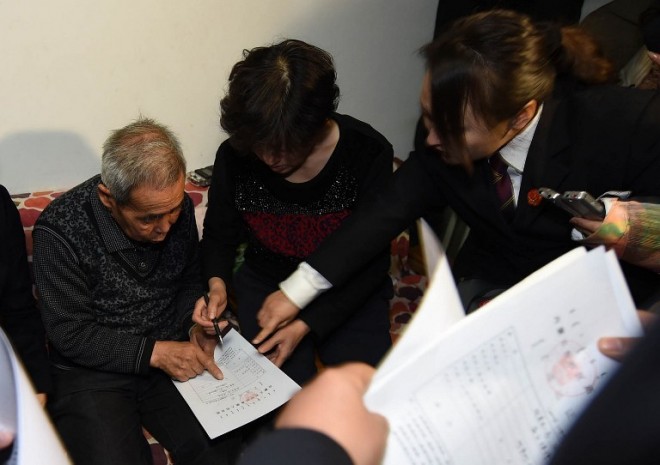 The judge of the higher people's court delivers retrial files to Hugjiltu's parents (C) in Hohhot, northern China's Inner Mongolia autonomous region on December 15, 2014. A Chinese teenager executed after being convicted of murder and rape 18 years ago was declared innocent by a court on December 15, in a rare overturning of a wrongful conviction. The 18-year-old, named Hugjiltu and also known as Qoysiletu, was found guilty and put to death in Inner Mongolia in 1996, but doubt was cast on the verdict when another man confessed to the crime in 2005.   CHINA OUT    AFP PHOTO