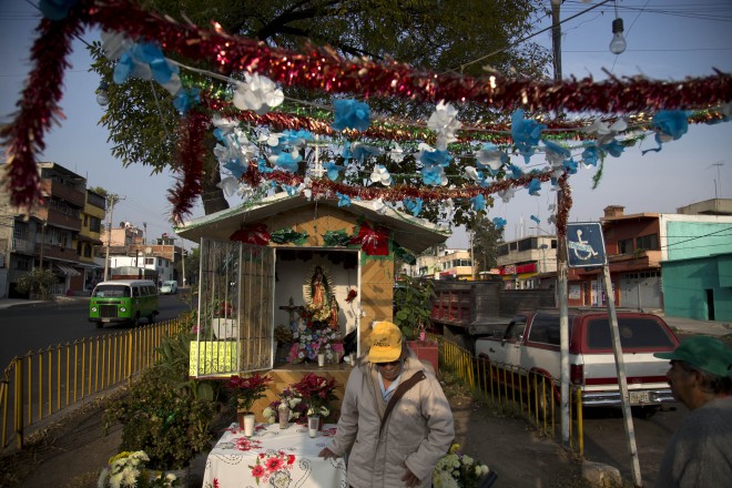 A man stands next to a neighborhood shrine to the Virgin of Guadalupe built on a street median in Mexico City, Friday Dec. 12, 2014. Every year thousands upon thousands of faithful flock to the Basilica of Guadalupe to pay their respects but just as importantly, little shrines built in parking lots, places of work, street medians, playgrounds and any imaginable corner of a world of concrete and asphalt are colorfully decorated with flowers, balloons and confetti on the Virgin's feast day as neighbors gather around the altars to share a small breakfast, sing happy birthday to the Virgin, light fire-crackers and some just come to have a quiet prayer. AP