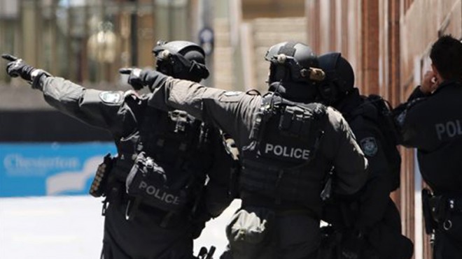 Armed police officers point as they stand at the ready close to a cafe under siege at Martin Place in Sydney, Australia, Monday, Dec. 15, 2014. A gunman took an unknown number of people hostage inside a downtown Sydney chocolate shop and cafe at the height of Monday morning rush hour, with two people inside the cafe seen holding up a flag believed to contain an Islamic declaration of faith.  AP PHOTO/ROB GRIFFITH