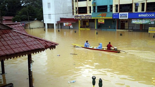 In this Wednesday, Dec. 24, 2014 photo, residents using a boat pass by flooded shops in Kuala Krai, Kelantan state, Malaysia. Malaysian Prime Minister Najib Razak said Friday, Dec. 26, 2014 he was cutting short his U.S. vacation to deal with the worst floods in the country in decades that have killed five people and displaced more than 100,000.  AP