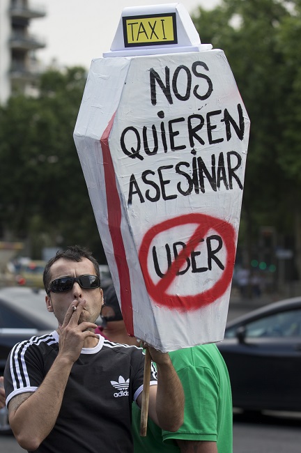 In this June 11, 2014 file photo, a demonstrator carries a mock coffin with a message reading 'They want to kill us - Uber' during a 24 hour taxi strike and protest in Madrid, Spain against unregulated competition from private companies, in particular, Uber. AP FILE PHOTO