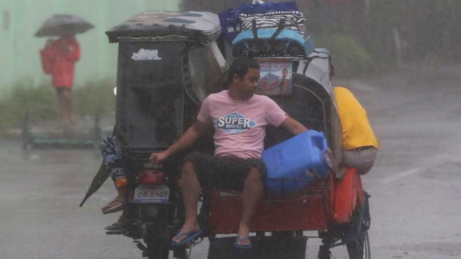 A resident rides a tricycle on their way to an evacuation center as strong winds and rains from Typhoon Hagupit hit Legazpi, Albay province, eastern Philippines on Sunday, Dec. 7, 2014. Typhoon Hagupit knocked out power in entire coastal provinces, mowed down trees and sent more than 650,000 people into shelters before it weakened Sunday, sparing the central Philippines a repetition of unprecedented devastation by last year's storm. (AP Photo/Aaron Favila)