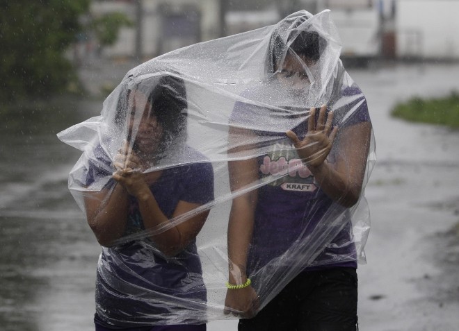 Filipino residents use plastic sheets to protect them from rains and strong winds brought by Typhoon Hagupit in Legazpi, Albay province, eastern Philippines on Sunday, Dec. 7, 2014. Typhoon Hagupit slammed into the central Philippines' east coast late Saturday, knocking out power and toppling trees in a region where 650,000 people have fled to safety, still haunted by the massive death and destruction wrought by a monster storm last year. (AP Photo/Aaron Favila)