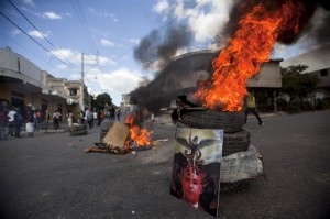 An image of Haiti's Prime Minister Laurent Lamothe stands against burning tires placed by anti-government protesters calling for his resignation, along with that of Haiti's President Michel Martelly in Port-au-Prince, Haiti. AP