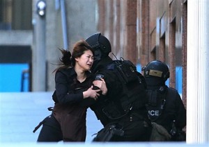 In this Dec. 15, 2014 photo, a hostage runs to armed tactical response police officers for safety after she escaped from a cafe under siege at Martin Place in the central business district of Sydney, Australia. AP