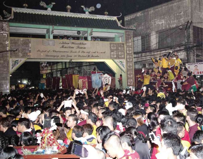 TWO FAITHS MEET  The Black Nazarene image and its swarm of Catholic devotees approach the sarimanok-motiffed gateway to Globo de Oro Street, a Muslim neighborhood in Quiapo, Manila. ALEXIS CORPUZ 