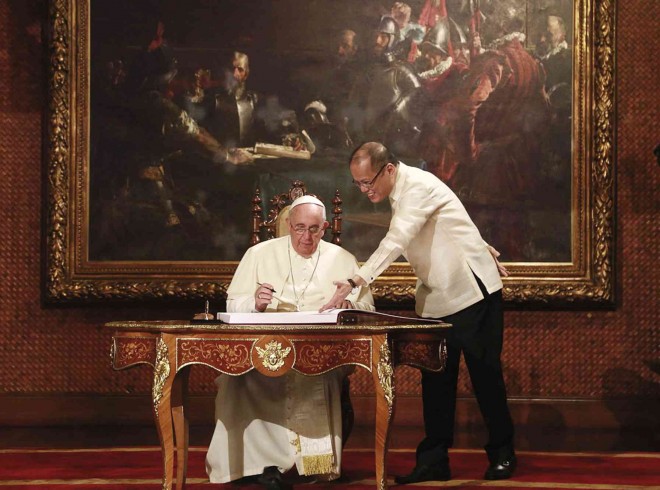 HONORED GUEST President Aquino holds down a page of the Palace guest book that Pope Francis was signing at the Reception Hall of Malacañang on  Friday morning.  The meeting of the two world leaders seemed to echo the spirit of Juan Luna’s painting “Blood Compact,” which hangs behind them. RYAN LIM/MALACAÑANG PHOTO BUREAU 