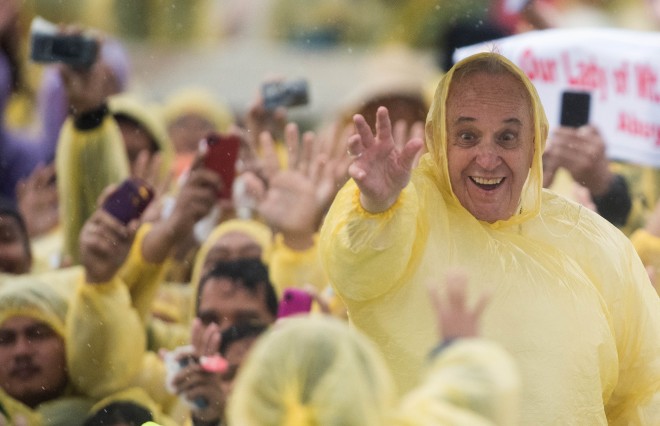Pope Francis (R) wears a plastic poncho as he waves to well wishers after a mass in Tacloban on January 17, 2015. Pope Francis will spend an emotional day in the Philippines on January 17 with survivors of a catastrophic super typhoon that claimed thousands of lives, highlighting his concern over climate change. AFP 