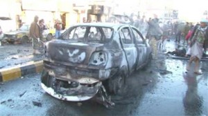 In this framegrabbed image from footage shot by AP Television News, a damaged car sits in the road after a suicide bomber driving a minibus full of explosives killed more than a dozen people Wednesday morning near a police academy in the heart of Yemen's capital, Sanaa, security officials said Wednesday Jan. 7, 2015. The blast wounded dozens more, officials said (AP Photo)
