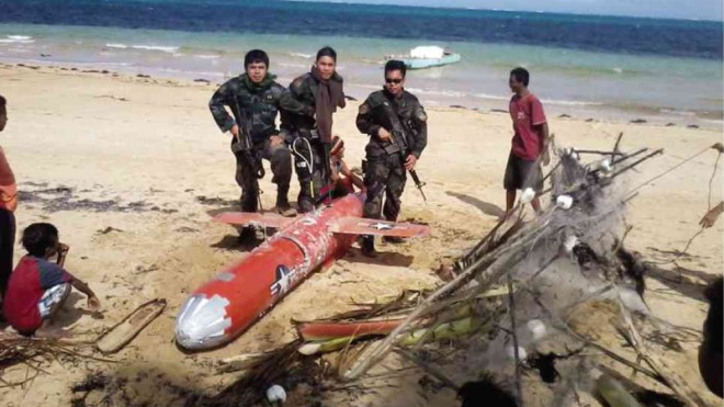 PHILIPPINE soldiers guard what is believed to be a surveillance drone, but which the US government said is an aerial target, which was found in the island town of Patnanungan in Quezon province on Sunday. Photo FROM FACEBOOK PAGE OF PATNANUNGAN POLICE