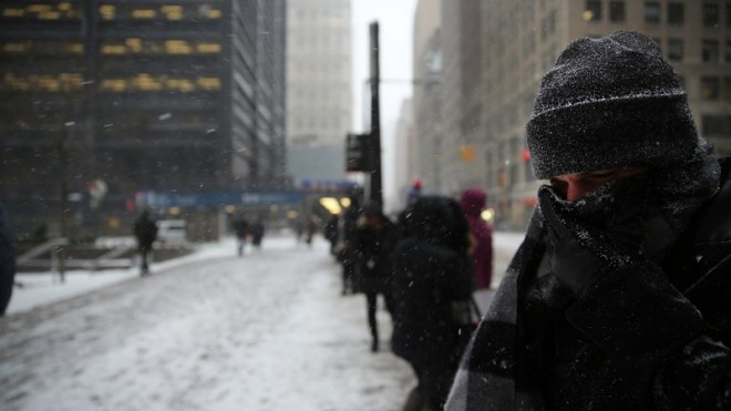 A man who has been waiting over two hours for a city bus covers his face during heavy snow in the financial district of Manhattan on January 26, 2015 in New York City. New York, and much of the Northeast, is bracing for a major winter storm which is expected to bring blizzard conditions and 18 to 24 inches of snow to the area.  SPENCER PLATT/GETTY IMAGES/AFP