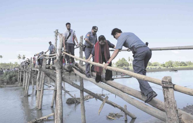 WALKING IN THEIR SHOES  A policeman helps Commission on Human Rights Chairperson Etta Rosales cross a wooden bridge on Wednesday, at the site of the encounter between members of the Special Action Force and Moro rebels. Rosales heads the investigation of reported excesses against civilians during the Mamasapano clash that left 44 police commandos, 18 rebels and four civilians dead on Jan. 25 in Mamasapano town, Maguindanao province.  JEOFFREY MAITEM/ INQUIRER MINDANAO