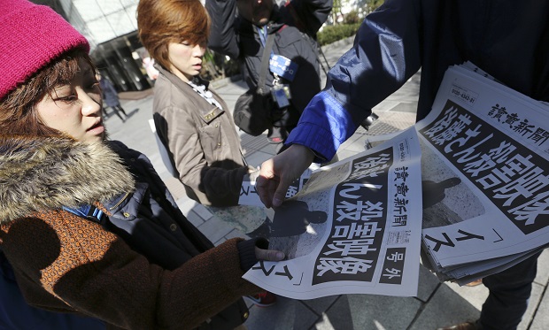 Passersby react as they receive extra newspapers in Tokyo reporting about an online video that purported to show an Islamic State group militant beheading Japanese journalist Kenji Goto,  Sunday morning, Feb. 1, 2015. Japan condemned with outrage and horror on Sunday after the video was posted on militant websites late Saturday Middle East time. The headline reads: "A video on killing of Goto." (AP Photo/Eugene Hoshiko)