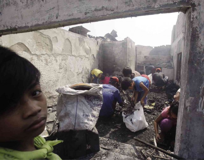 SOOTY SALVAGE Malabon City residents on Wednesday pick through the debris for reusable items following the eight-hour fire that displaced 700 families. AP 