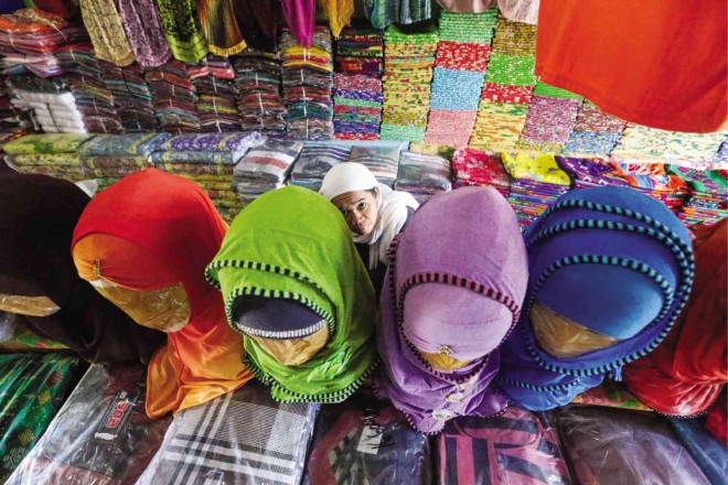 COLORS OF PEACE  A woman peeks from a row of mannequins garbed in the happy colors of the  hijab inside a stall at the Barter Trade Center in Cotabato City. The center is known for selling locally handwoven fabrics as well as textiles imported from Indonesia, Malaysia and Thailand in colors that might as well be the colors of peace when it dawns on Mindanao.  REM ZAMORA 