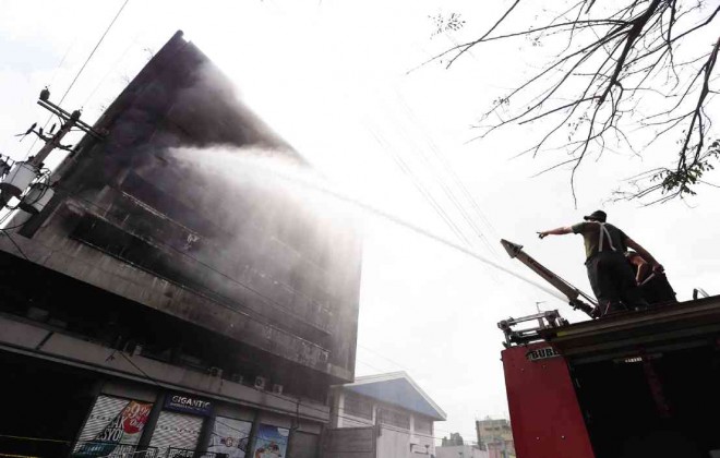 Firemen shoot water into the upper floors of Gateway 2000 Development Corp., a building on Araneta Avenue, Quezon City, which caught fire shortly around midnight Saturday. At 4 p.m. yesterday, smoke was still rising from the structure full of highly combustible materials.  Lyn Rillon