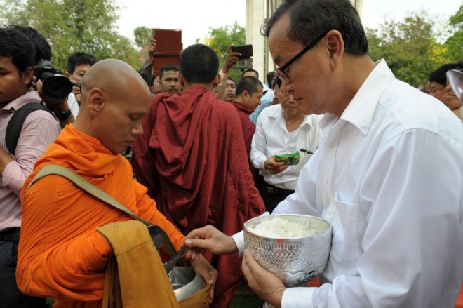 Cambodian opposition party leader Sam Rainsy (R) offers food to a Buddhist monk at Choeung Ek killing fields memorial in Phnom Penh on April 17, 2015. Tearful survivors on April 17, 2015 marked 40 years to the day since the black-clad Khmer Rouge marched into Phnom Penh, ending a civil war but heralding a terror that killed a quarter of Cambodians and turned the capital into a ghost town. AFP PHOTO / TANG CHHIN SOTHY