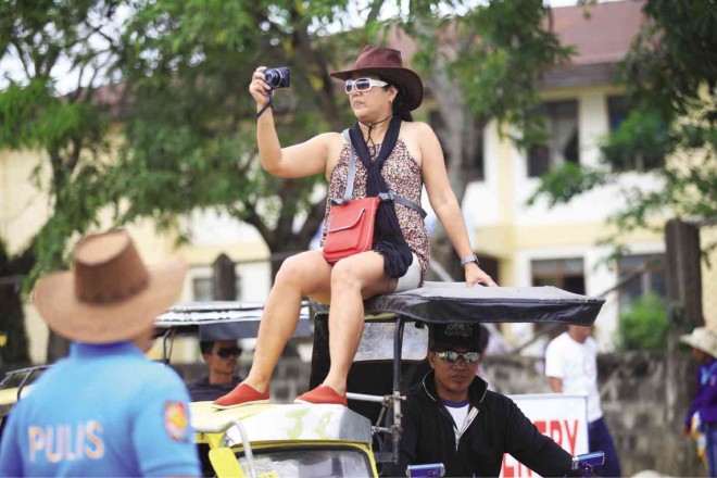 A tourist takes shots of activities on top of a tricycle during the cattle drive in Masbate City. 