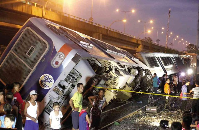 PEOPLE gawk at two coaches of a Philippine National Railways train which fell over as it was traveling southbound in Taguig City on Wednesday afternoon.  The cause of the derailment has yet to be determined. Marianne Bermudez